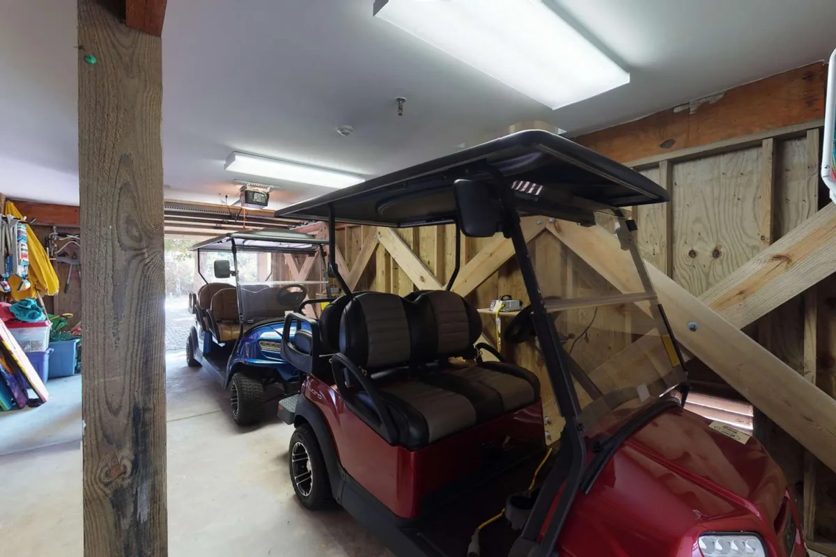This image showcases a garage space featuring two golf carts parked under wooden beams, with organized storage visible in the background. The setting is practical and inviting, highlighting the convenience offered to guests for island exploration.