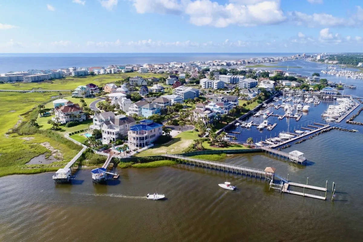 A view of waterfront houses lining a tranquil marina, boats docked along the water, lush green open spaces, and inviting walking paths weaving through the neighborhood. The marina is bustling with activity, and the scene captures the lively yet relaxing atmosphere of the island’s main hub.