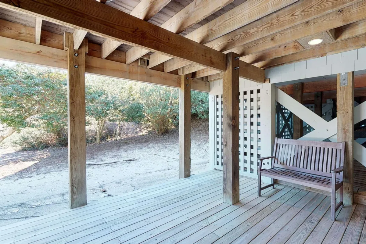 This exterior image captures a wooden bench set on a deck or porch, surrounded by sturdy support beams and lush views of nature just outside. The atmosphere is tranquil, suggesting a versatile space for both relaxation and gathering, with the potential for sunrise or sunset views and gentle breezes.