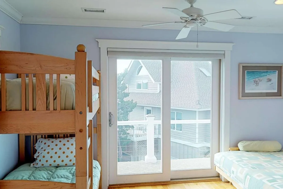 A cozy bunk room with decorative artwork, featuring bunk beds and a sliding glass door that leads directly to an outdoor balcony or deck. The space is designed for comfort and fun, ideal for children or groups, with a view suggesting easy outdoor access.