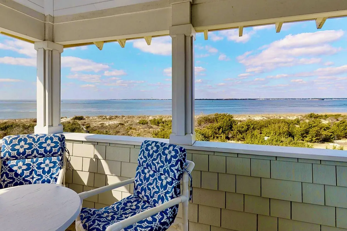 A stylish deck setup featuring blue patterned chairs and a white table overlooking the ocean. The scene exudes tranquility, with seating positioned to maximize enjoyment of the panoramic Atlantic view, ideal for reading, sipping drinks, or simply unwinding to the sound of the waves.