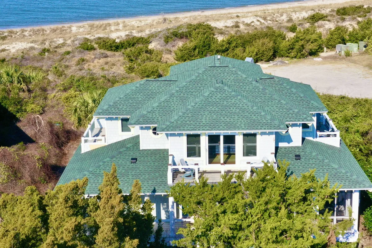 This image presents a spacious deck with a green roof, surrounded by lush greenery and offering a clear view of the ocean. Multiple seating arrangements are visible, ideal for gatherings or quiet relaxation. The openness of the deck invites fresh air and sunlight, perfectly reflecting a seamless indoor-outdoor experience.
