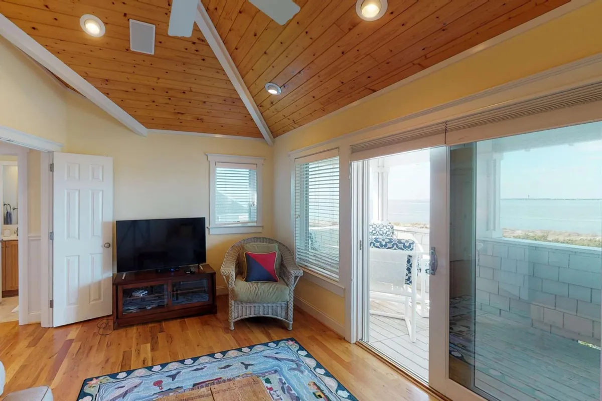 A cozy living space highlighted by a comfortable chair, flat-screen TV, and large windows opening to a patio. The view captures the transition from indoors to the outdoor deck, with sunset light streaming in.